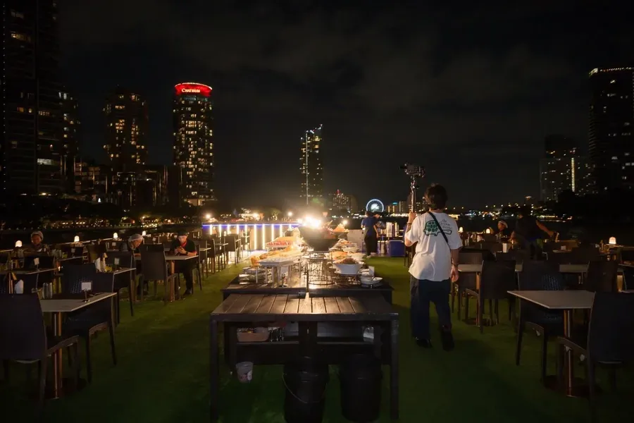 โต๊ะอาหารและไลน์บุฟเฟต์บนดาดฟ้า Alangka Cruise พร้อมวิวอาคารริมแม่น้ำยามค่ำคืน