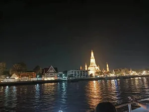 วัดอรุณประดับไฟยามค่ำคืน มีแสงสะท้อนบนแม่น้ำเจ้าพระยา มองจากบนเรือ