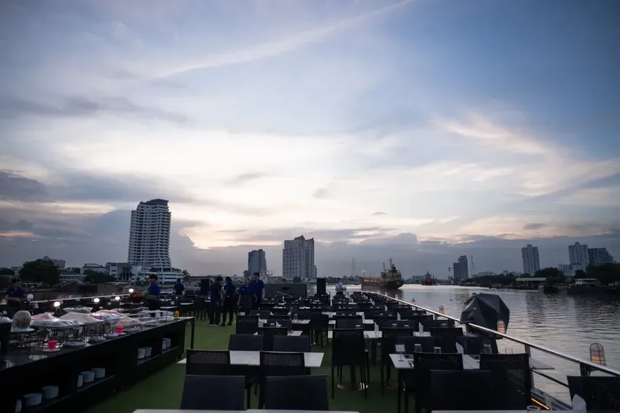 โต๊ะอาหารบนดาดฟ้าเปิดโล่งของเรือ Alangka Cruise พร้อมวิวแม่น้ำเจ้าพระยาช่วงเย็น