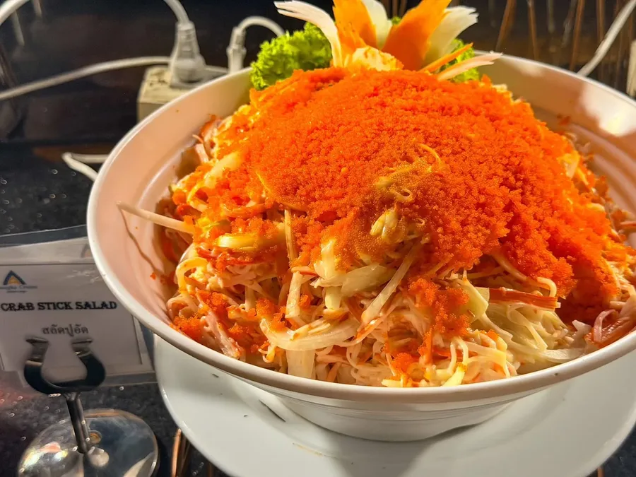 สลัดปูอัดในชามสีขาว โรยหน้าสีส้มและตกแต่งด้วยผักแกะสลัก