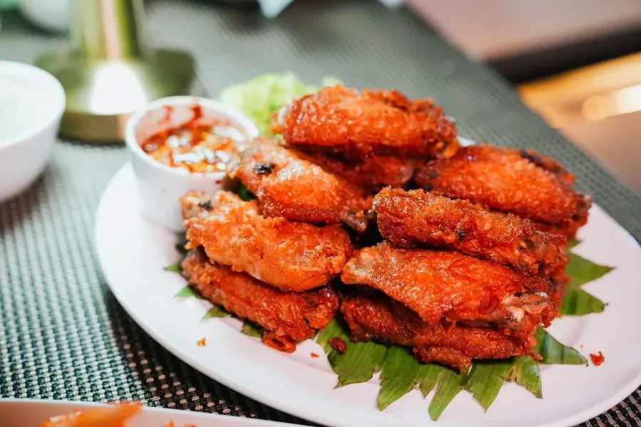 ปีกไก่ทอดสีน้ำตาลทองบนจานรองใบตอง เสิร์ฟคู่ถ้วยน้ำจิ้ม
