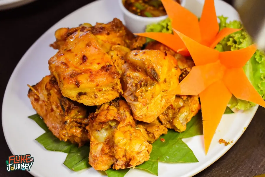 ไก่สีเหลืองทองจัดบนจานรองใบตอง พร้อมน้ำจิ้มและแครอตแกะสลัก