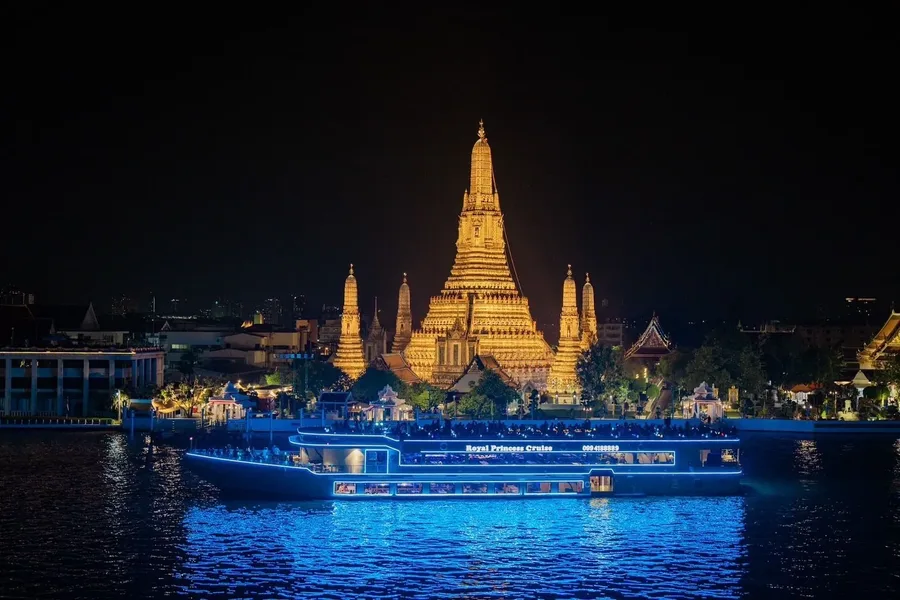 ชมความงดงามของวัดอรุณยามค่ำคืน พระปรางค์สีทองตัดกับแสงสีน้ำเงินของเรือและเงาสะท้อนบนสายน้ำ