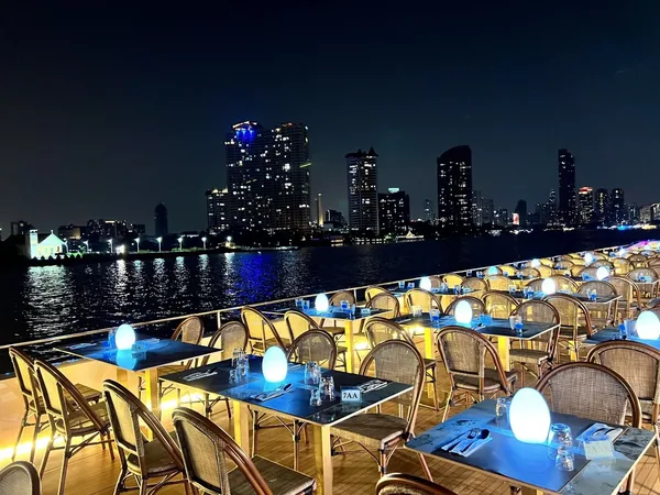 โซนดาดฟ้าริม The Planet Cruise พร้อมโต๊ะที่นั่งแบบ Open Air และวิวเมืองริมแม่น้ำเจ้าพระยายามค่ำคืน