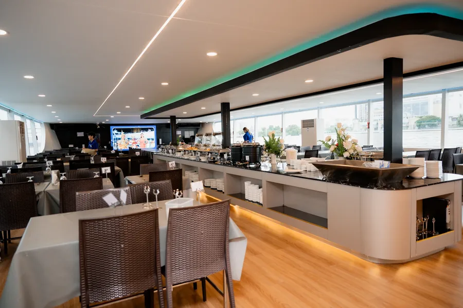 ห้องอาหารบนเรือ Unicorn Cruise จัดโต๊ะนั่งข้างเคาน์เตอร์บุฟเฟต์แนวยาว พร้อมหน้าต่างกระจกบานใหญ่ที่มองเห็นวิวแม่น้ำเจ้าพระยา