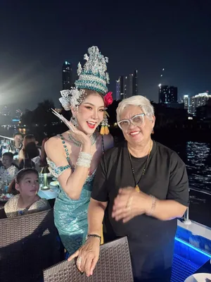 ผู้โดยสารสวมแว่นถ่ายภาพกับนักแสดงชุดสีฟ้าประดับเครื่องศีรษะบนเรือ Unicorn มีวิวแม่น้ำด้านหลัง
