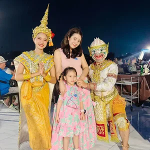 ผู้หญิงและเด็กถ่ายภาพกับนักแสดงชุดไทยสีทองและนักแสดงหนุมานบนเรือ Unicorn ยามค่ำคืน