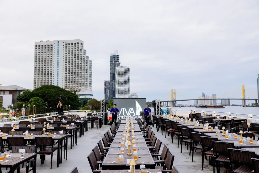 ชมบรรยากาศดาดฟ้าเปิดโล่งที่จัดโต๊ะอาหารเป็นระเบียบ ทั้งโต๊ะยาวกลางลำและโต๊ะสองฝั่ง พร้อมวิวแม่น้ำและอาคารริมฝั่ง