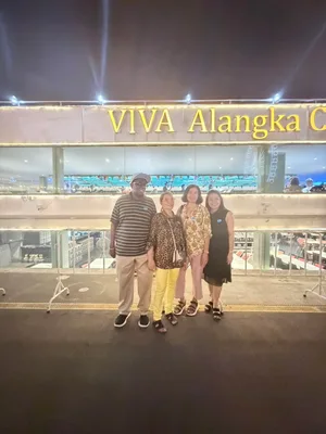 ผู้โดยสารสี่คนถ่ายภาพบริเวณท่าเรือด้านหน้าเรือ Viva Alangka Cruise ที่ประดับไฟยามค่ำคืน