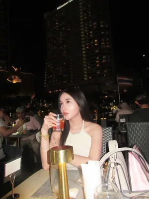 ผู้โดยสารหญิงถือแก้วเครื่องดื่มที่โต๊ะอาหารบนเรือ Viva Alangka Cruise โดยมีอาคารริมแม่น้ำยามค่ำคืนเป็นฉากหลัง