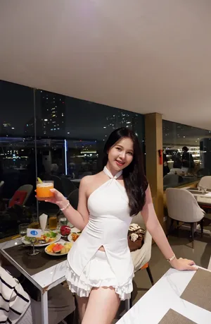 ผู้โดยสารหญิงสวมชุดสีขาวยิ้มให้กล้องและถือแก้วเครื่องดื่มสีส้มในห้องอาหารเรือ Viva Alangka Cruise