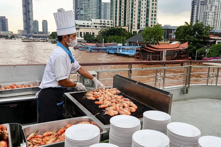ชมเชฟเตรียมกุ้งบนเตาย่างกลางแจ้ง ท่ามกลางวิวแม่น้ำและอาคารริมฝั่ง เติมความอร่อยให้มื้ออาหารบนเรือ